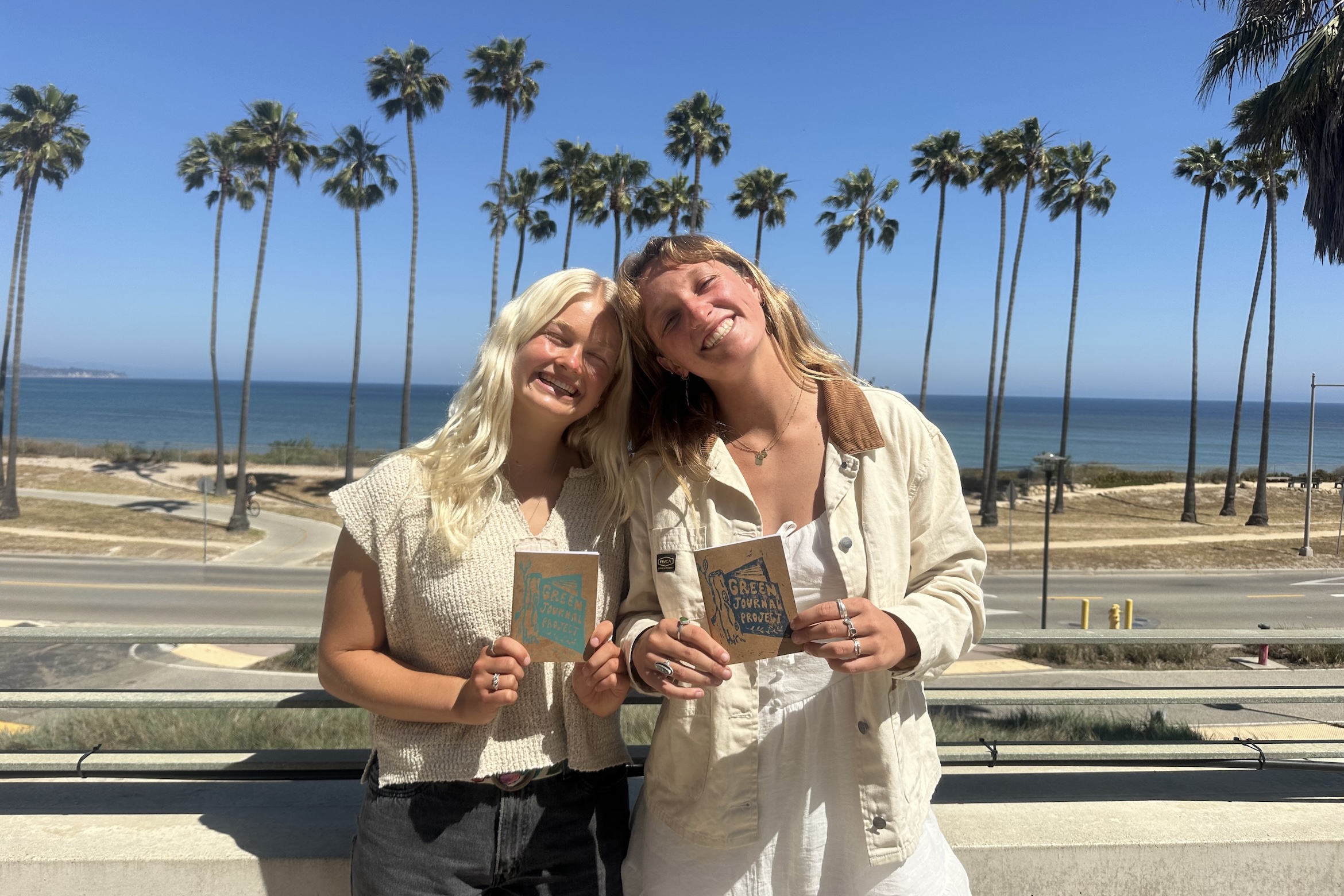 Two students standing in front of the ocean holding nature journals